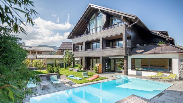 Une maison moderne à deux étages, dotée d’une piscine, d’une terrasse en bois et d’un jardin bien entretenu.
