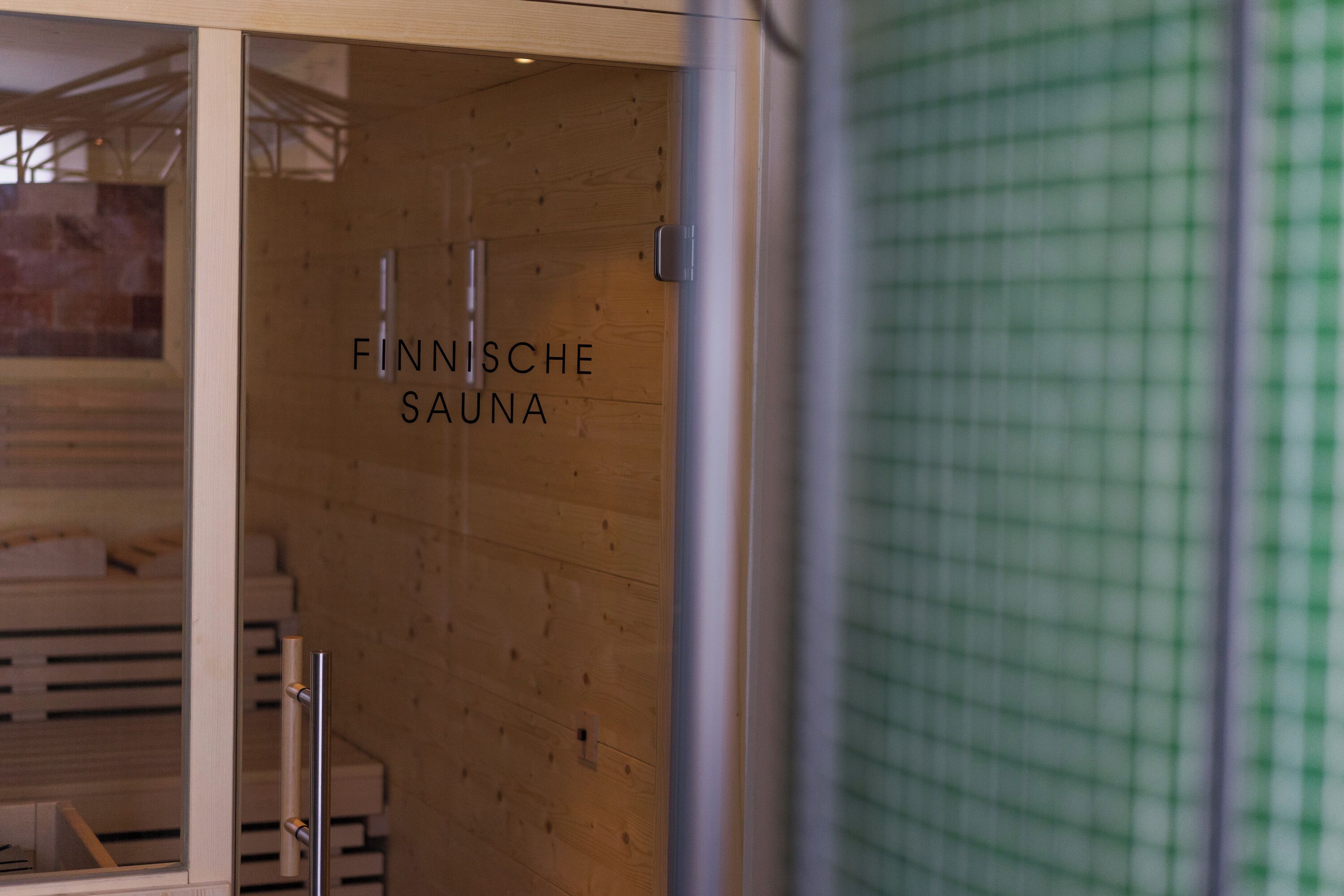 Interior de una sauna de madera con una puerta de vidrio y el texto 'FINNISCHE SAUNA' a la vista.
