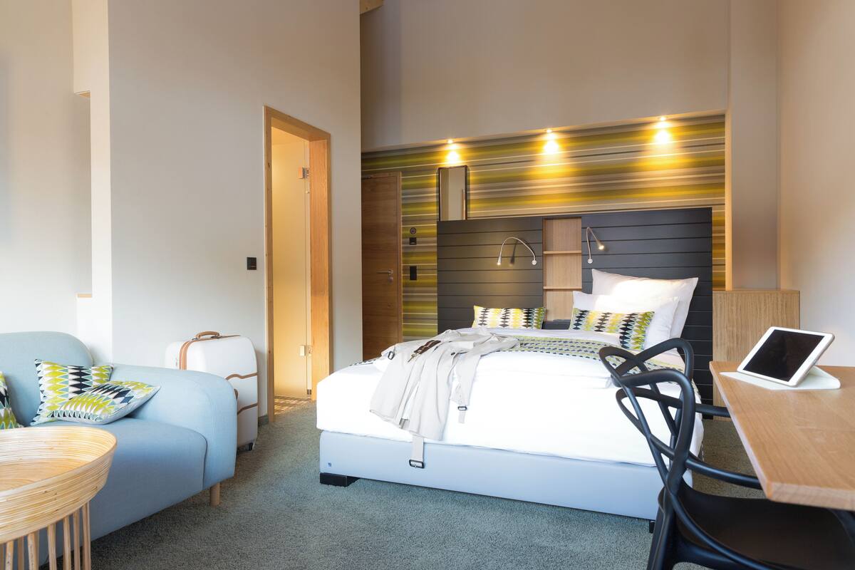 Una habitación de hotel moderna con una cama, un escritorio, una silla, una maleta y una mesita.
