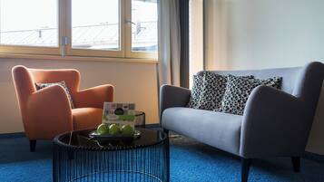 A room with a blue carpet, a grey sofa, an orange armchair, and a black coffee table with a magazine and apples.