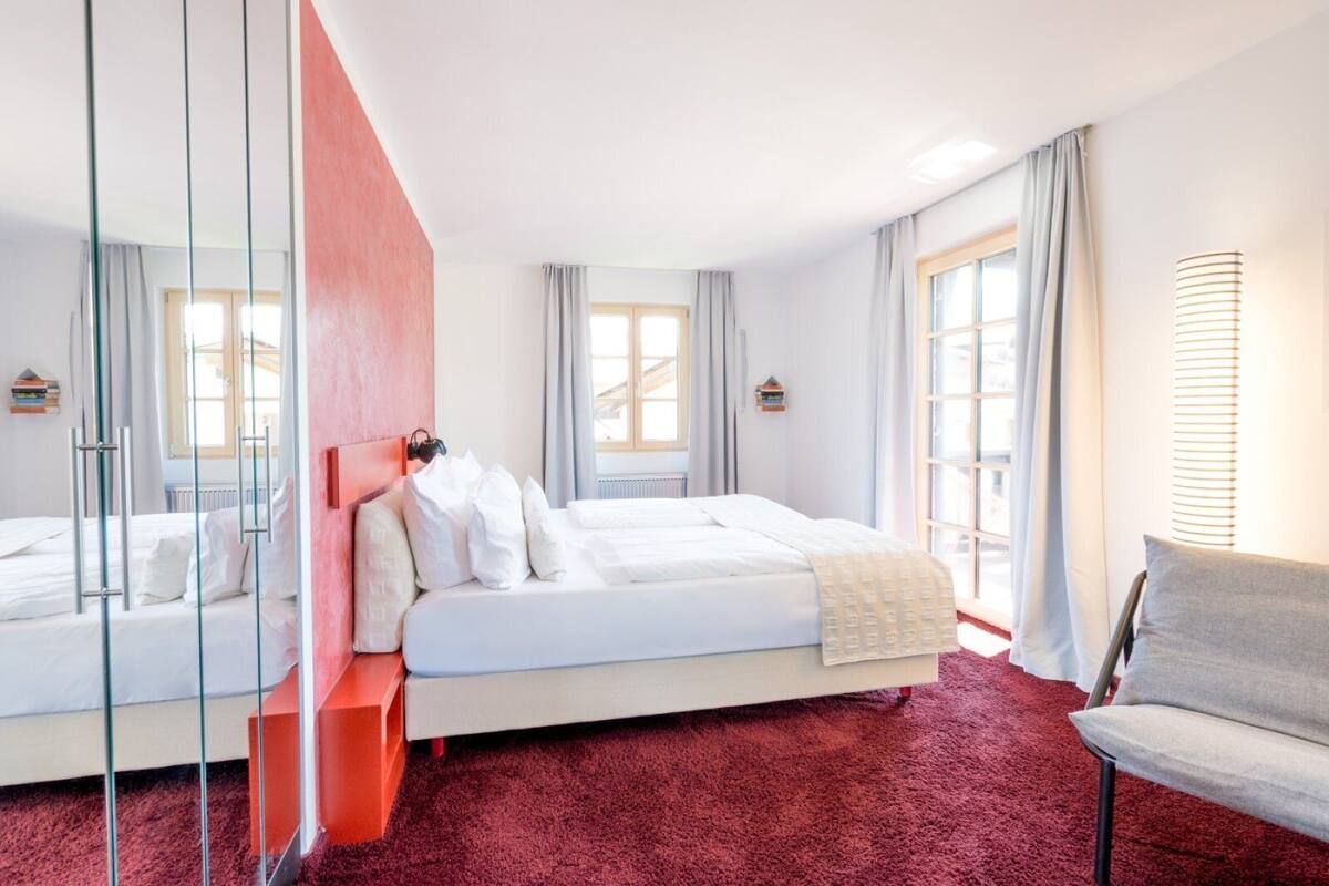 Una habitación de hotel moderna con una cama grande, una zona de estar con una silla y un separador de vidrio.