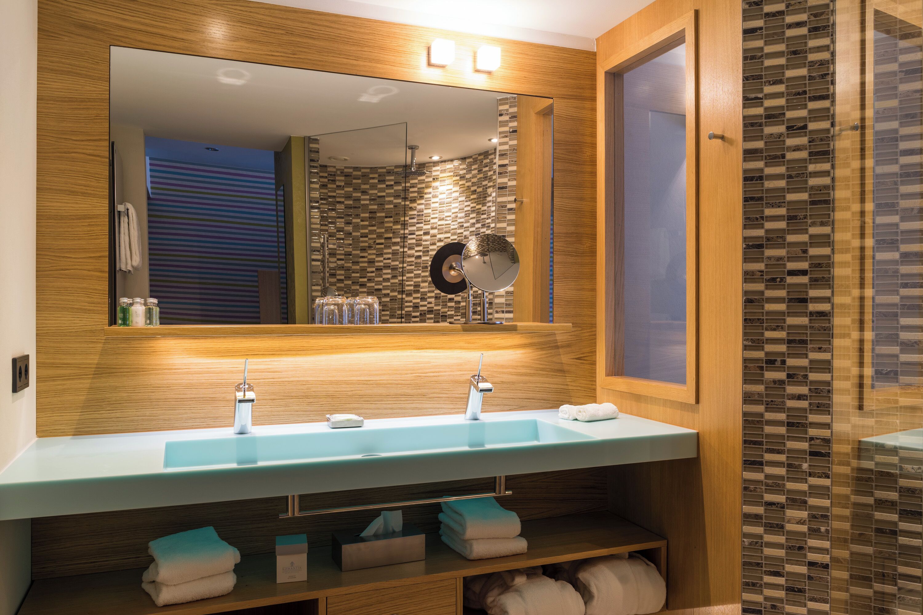 A modern bathroom with a large mirror, two sinks, and a shower area.
