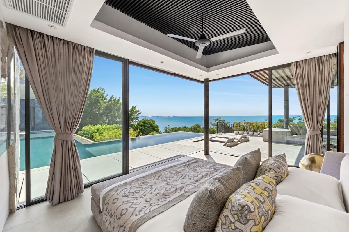Une chambre moderne avec un grand lit, une vue sur une piscine et un balcon aménagé avec du mobilier d’extérieur.