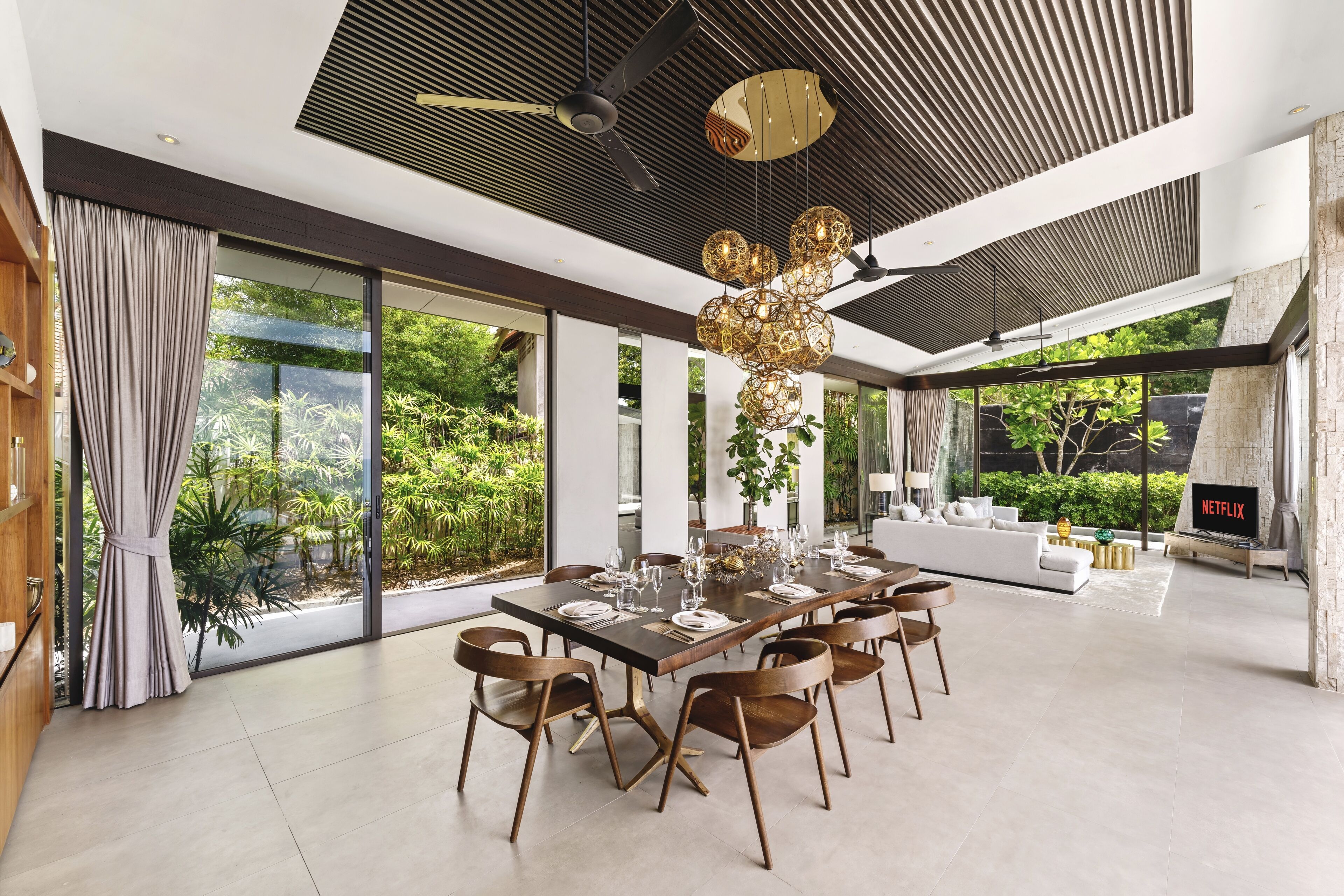 A modern dining area with a large table set for six, surrounded by wooden chairs.