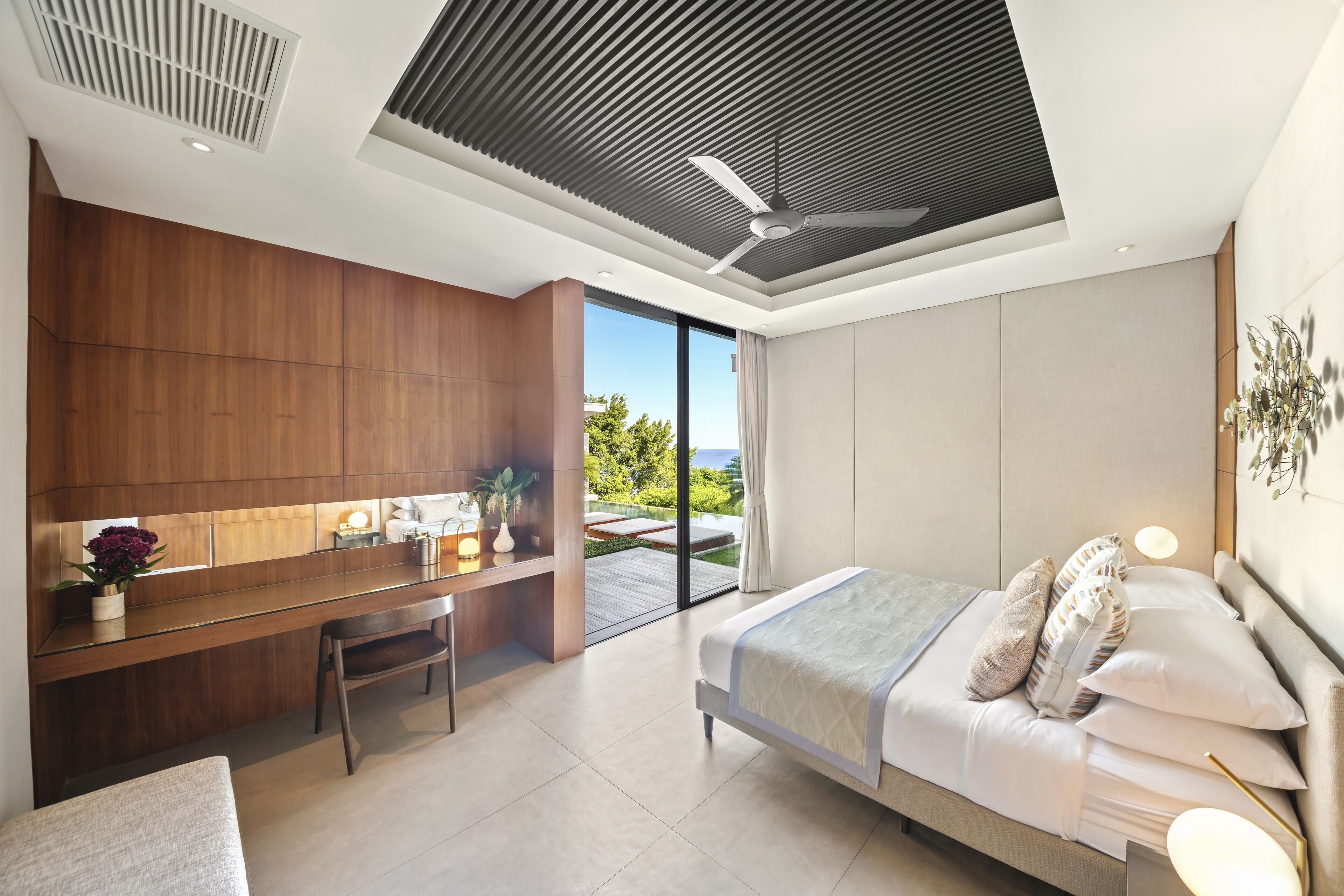 A modern bedroom with a large bed, a desk, and a view of the outdoors.