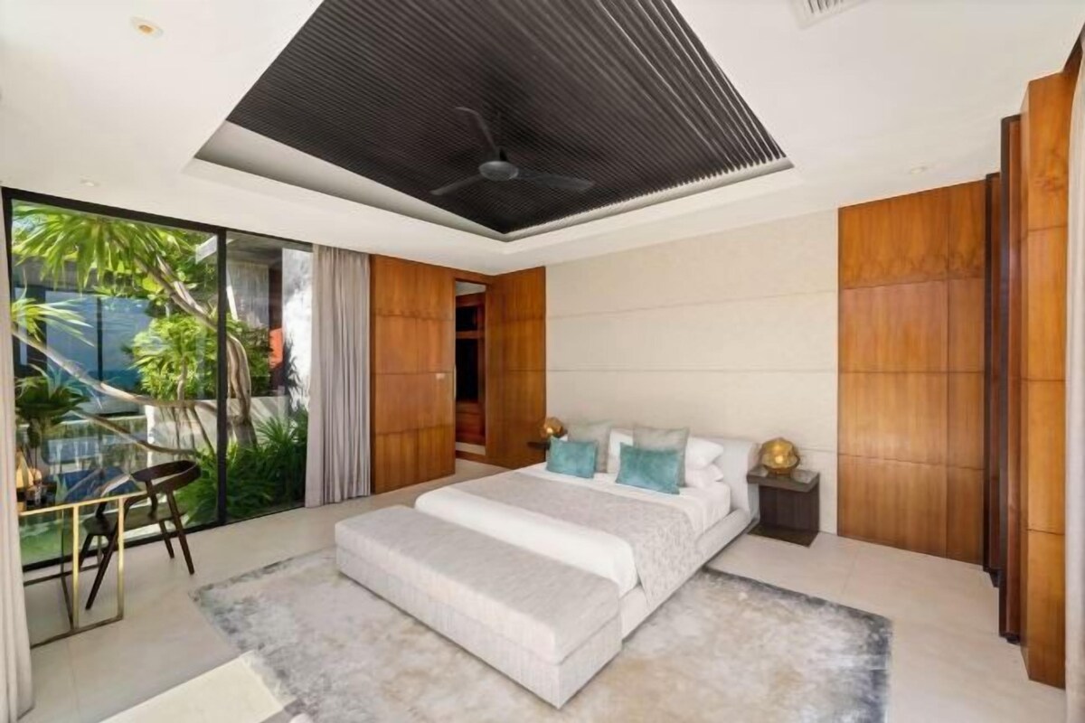 Quarto moderno com cama grande, ventilador de teto e vista para o verde lá fora.