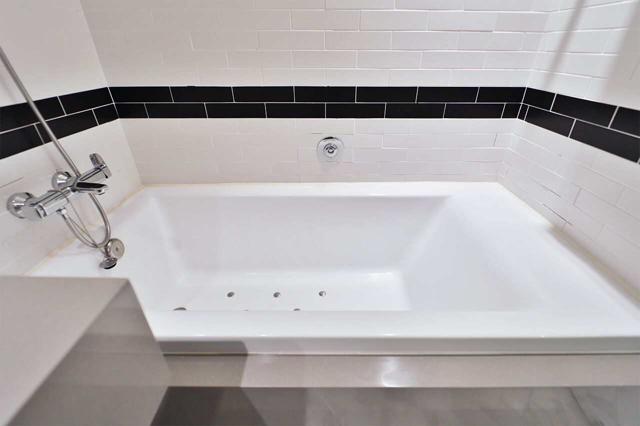 Un baño moderno con una bañera blanca, paredes con azulejos blanco y negro, y una ducha cromada.