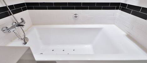 Un baño moderno con una bañera blanca, paredes con azulejos blanco y negro, y una ducha cromada.