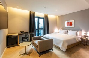 Una habitación de hotel moderna con una cama, un escritorio, una silla, una mesita y una ventana con cortinas.