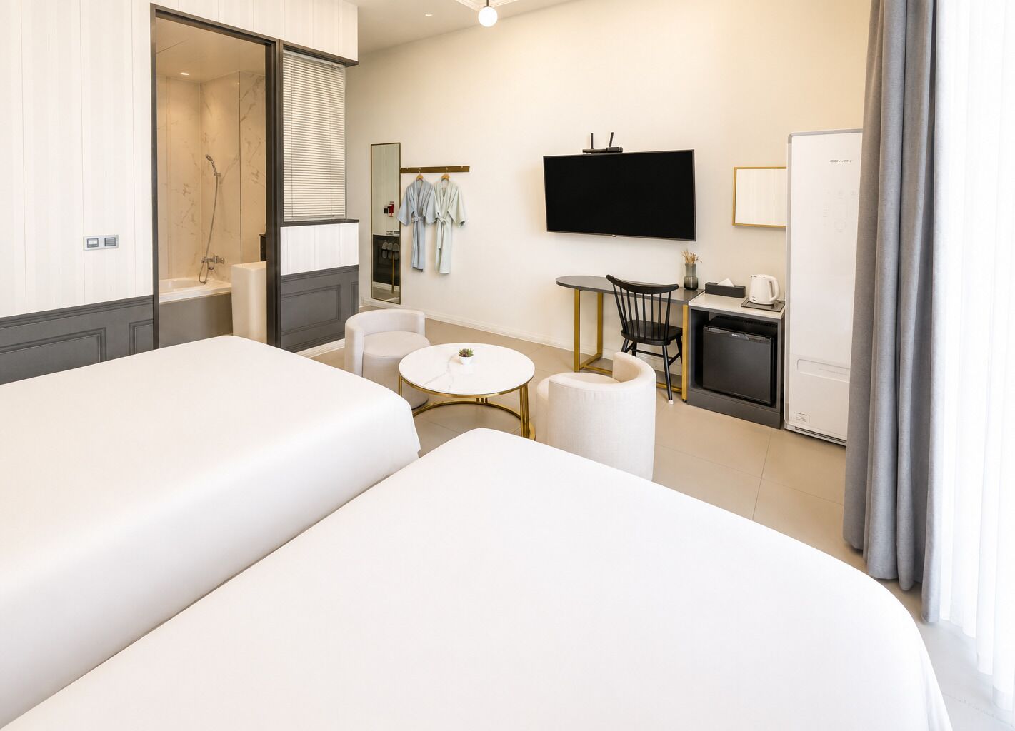 Habitación de hotel con dos camas, televisión, una mesita, una silla, escritorio con cafetera y minibar.