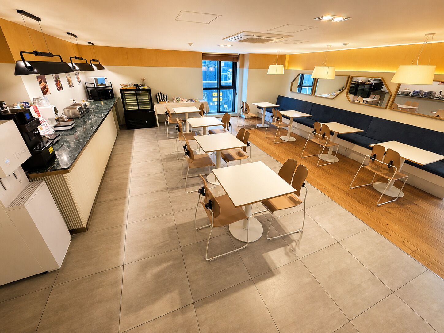 A modern cafe with multiple tables and chairs, a counter with a coffee machine, and a view of the street outside.