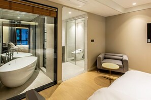 Una habitación de hotel moderna con una bañera grande, zona de ducha separada, sofá y una pequeña mesa.
