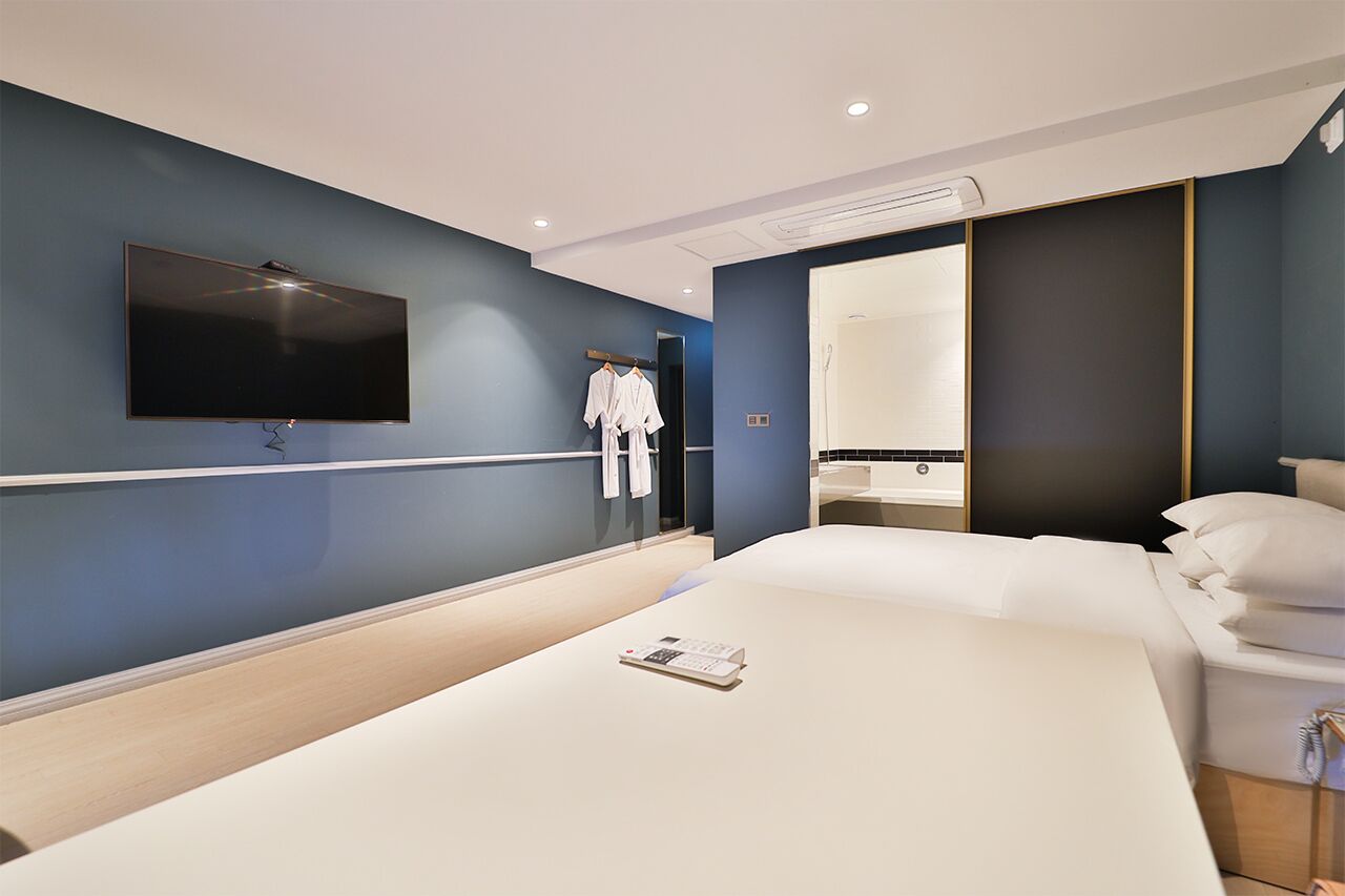 A modern hotel room with a large bed, a flat-screen TV mounted on the wall, and a large mirror.