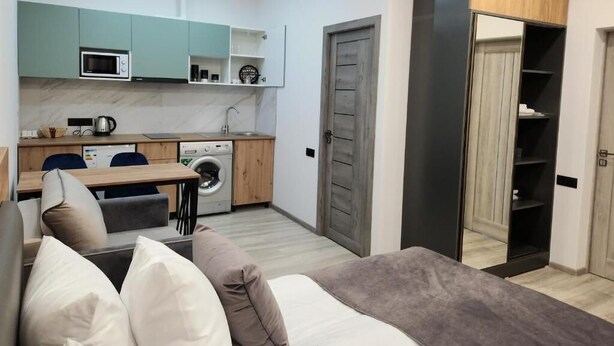 Un espacio habitable compacto con kitchenette, lavadora, sofá con cojines y armario con espejo.