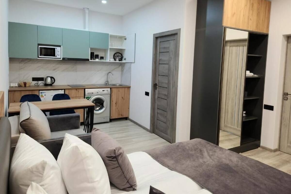 Ein kompakter Wohnraum mit Küchenzeile, Waschmaschine, einer Couch mit Kissen und einem Schrank mit Spiegel.