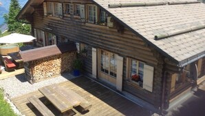 A wooden chalet with a sloped roof, a wooden deck, and a stone wall with firewood. - Charming log chalet at 1200 m – CAR-FREE, access by gondola only (Emmetten)