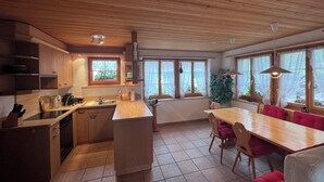 A kitchen with wooden cabinets, a sink, and a dining area with a table and chairs. - Charming log chalet at 1200 m – CAR-FREE, access by gondola only (Emmetten)