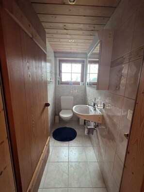 Un baño estrecho con inodoro, lavamanos y paredes de madera.