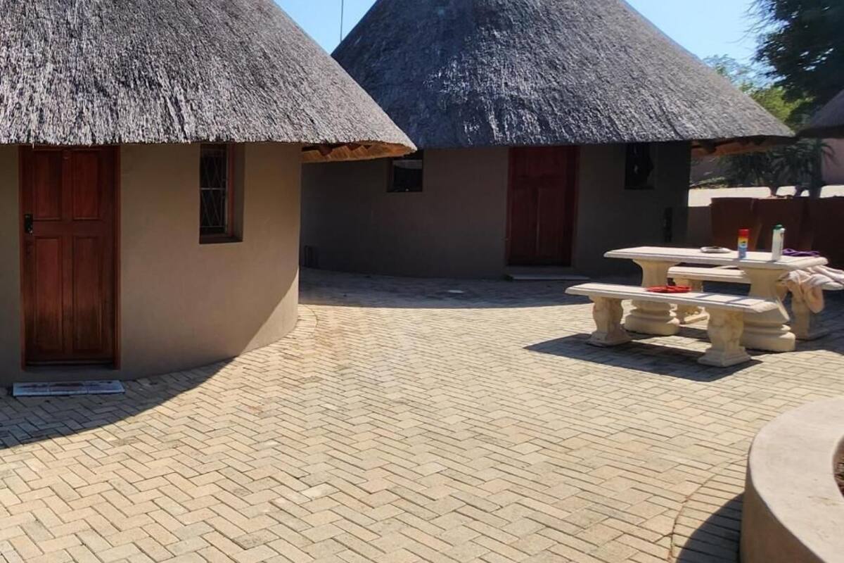A courtyard with thatched-roof huts, a paved walkway, and a stone bench.