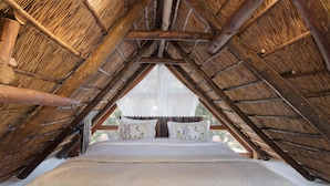 A bed in a room with a thatched roof and wooden beams. - La Ferme Guest Farm (Franschhoek)