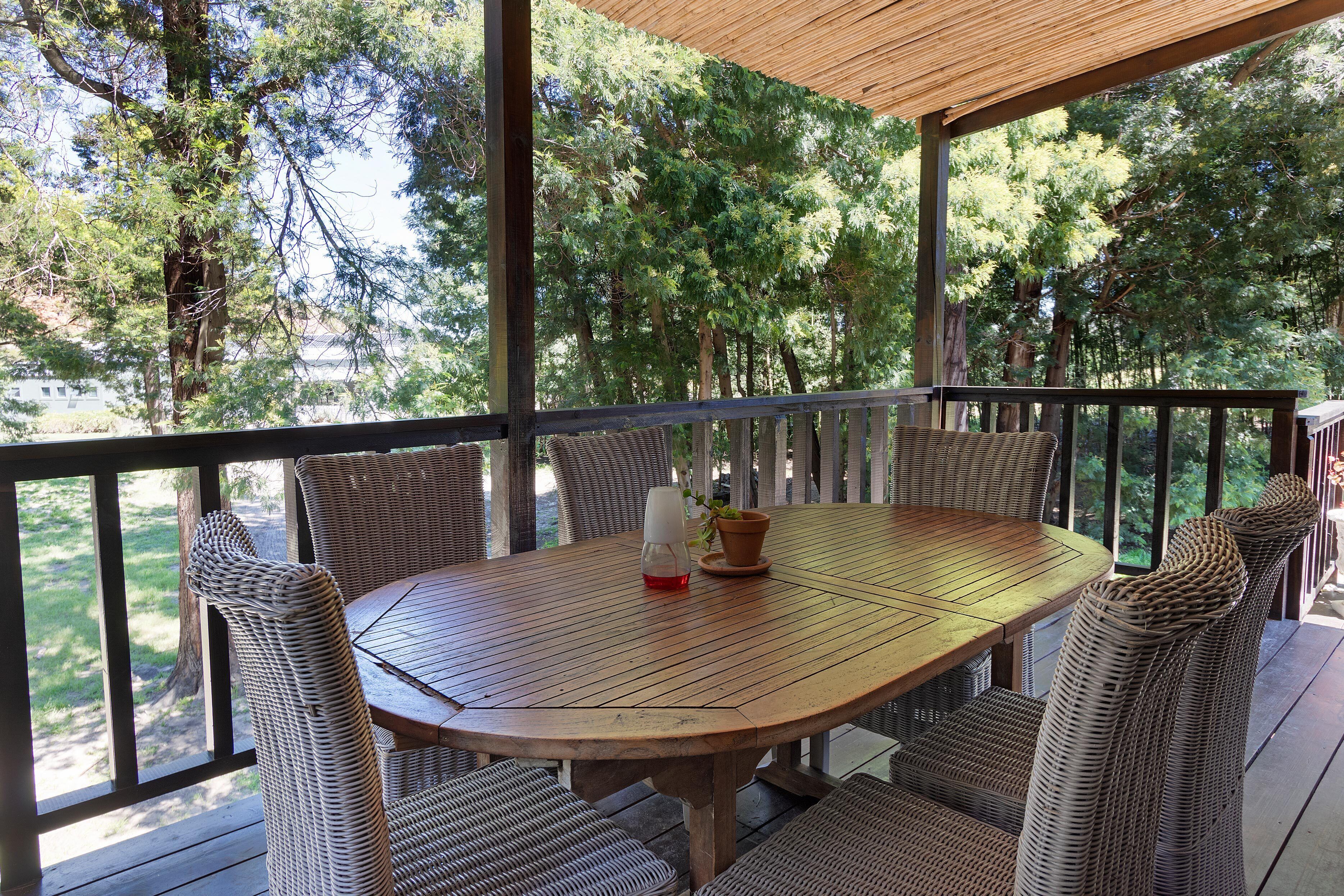 A covered outdoor patio with a round wooden table and wicker chairs.