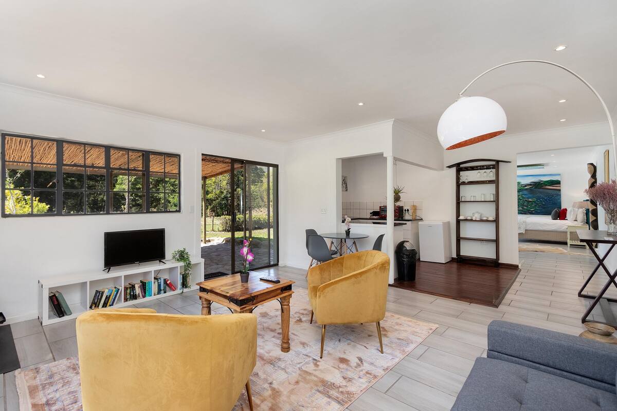 Een moderne woonkamer met een televisie, boekenplanken en gele fauteuils.