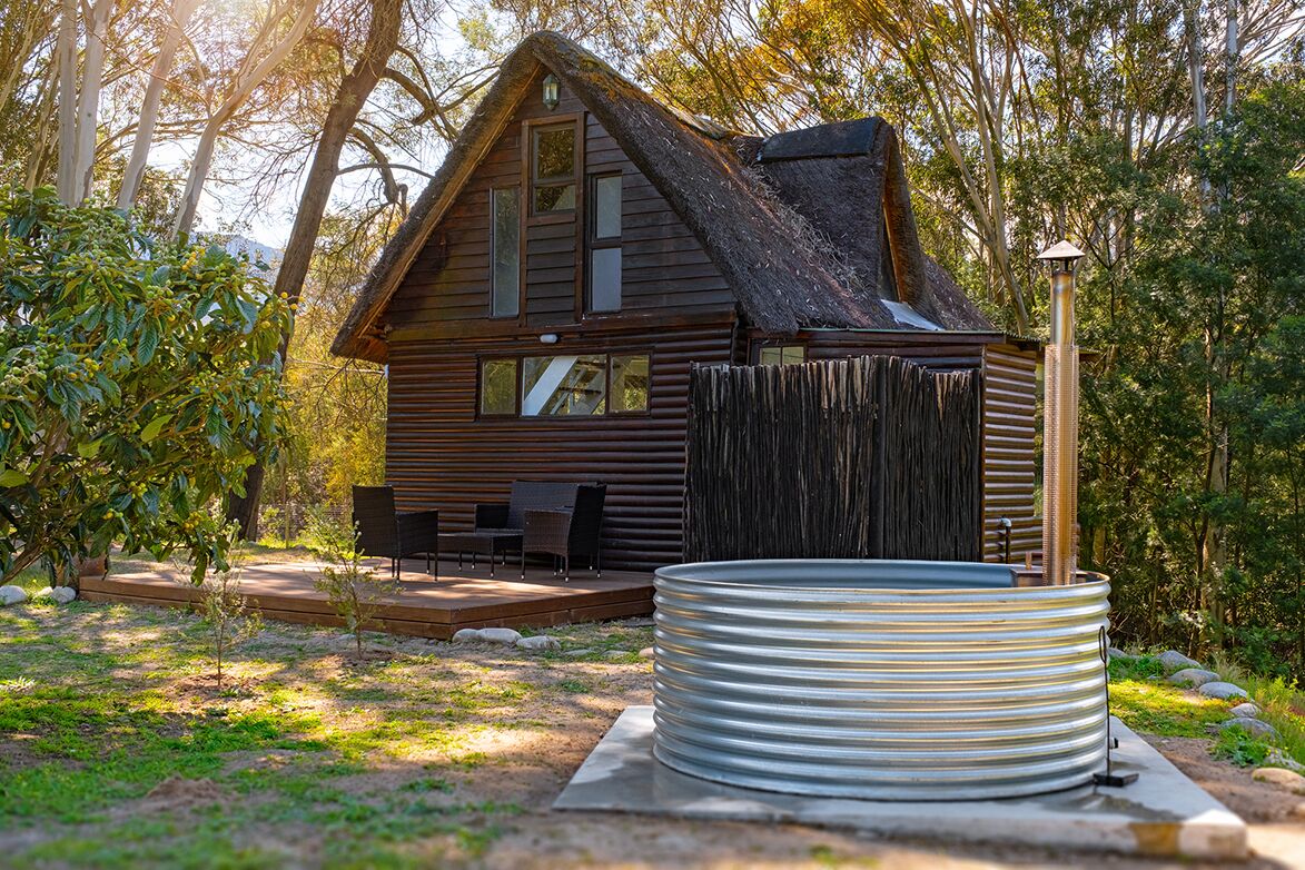 A rustic cabin with a thatched roof, a wooden deck, and a hot tub.