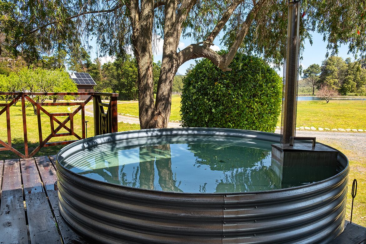 A hot tub with a metal frame, surrounded by a wooden deck, trees, and a solar panel in the background.