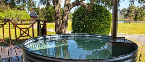 A hot tub with a metal frame, surrounded by a wooden deck, trees, and a solar panel in the background.