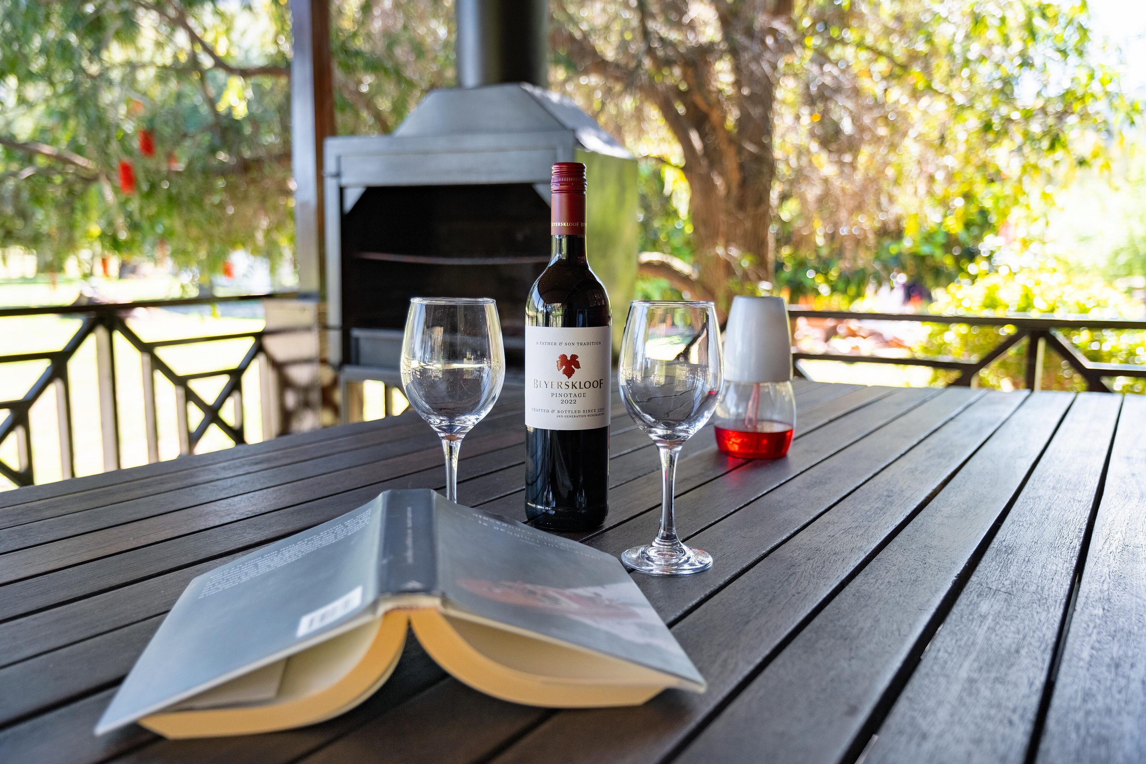 A table with a bottle of wine, two empty glasses, and an open book.