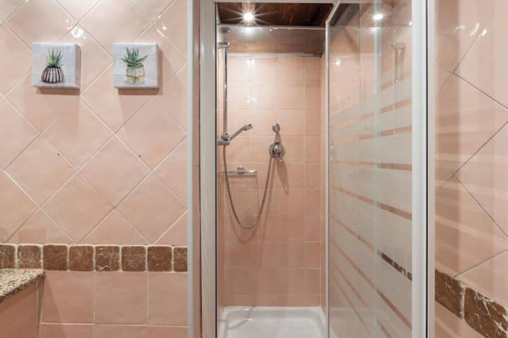 A glass-enclosed shower with a handheld showerhead and a wall-mounted faucet.