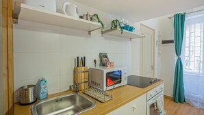 A compact kitchen with a sink, microwave, and stove, wooden countertop, and white cabinets. - Boutique apartment in the party street (Budapest)