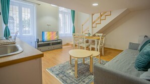 A modern living room with a grey sofa, wooden dining table, and chairs. A staircase leads to an upper level. - Boutique apartment in the party street (Budapest)