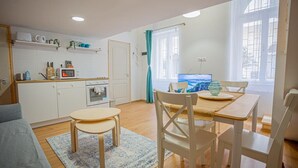 A compact living space with a kitchenette, a dining area with a table and chairs, a sofa, and a large window providing natural light. - Boutique apartment in the party street (Budapest)