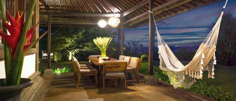 An outdoor patio with a wooden table and chairs, a hammock, and a view of the night sky.