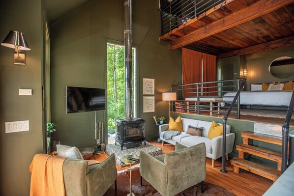 A cozy room with a sofa, chairs, a fireplace, a TV, and a staircase leading to a loft bed area.