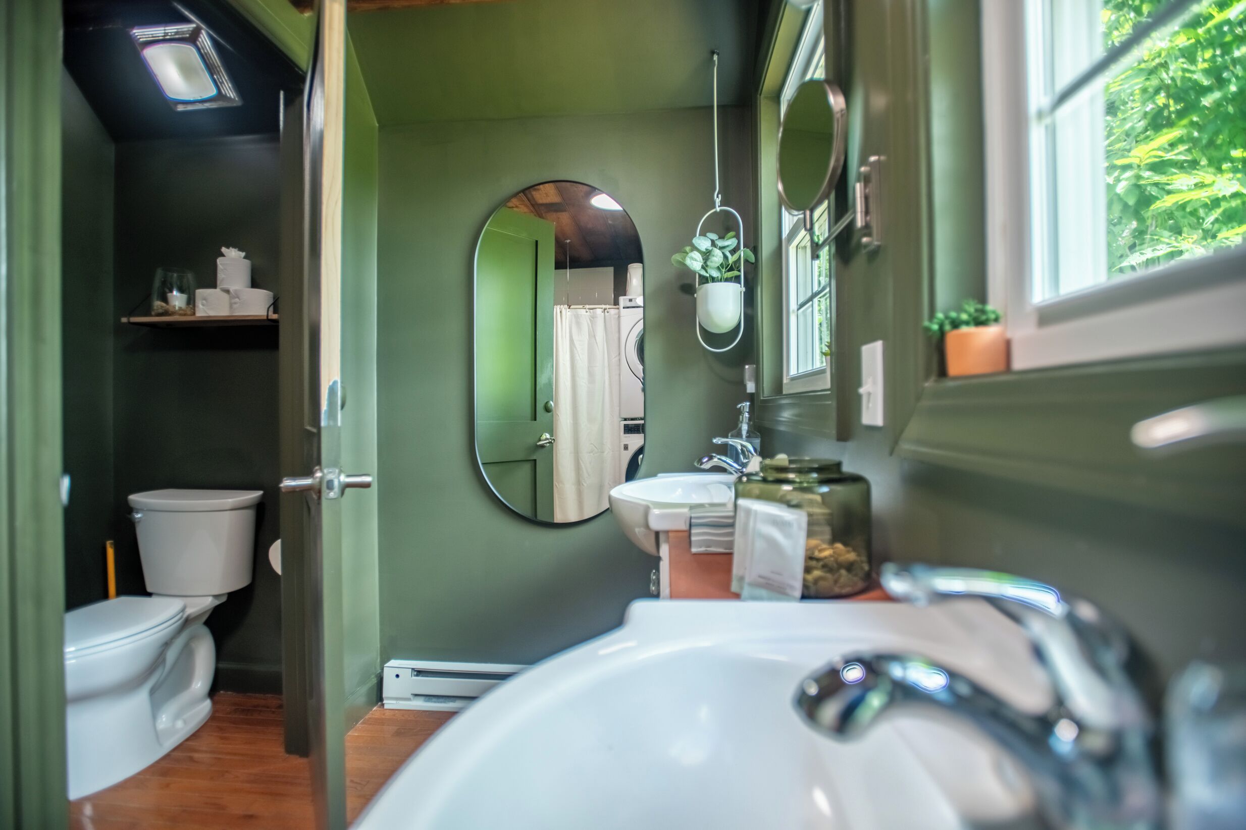 Un baño con inodoro, lavabo, espejo y una planta colgante.