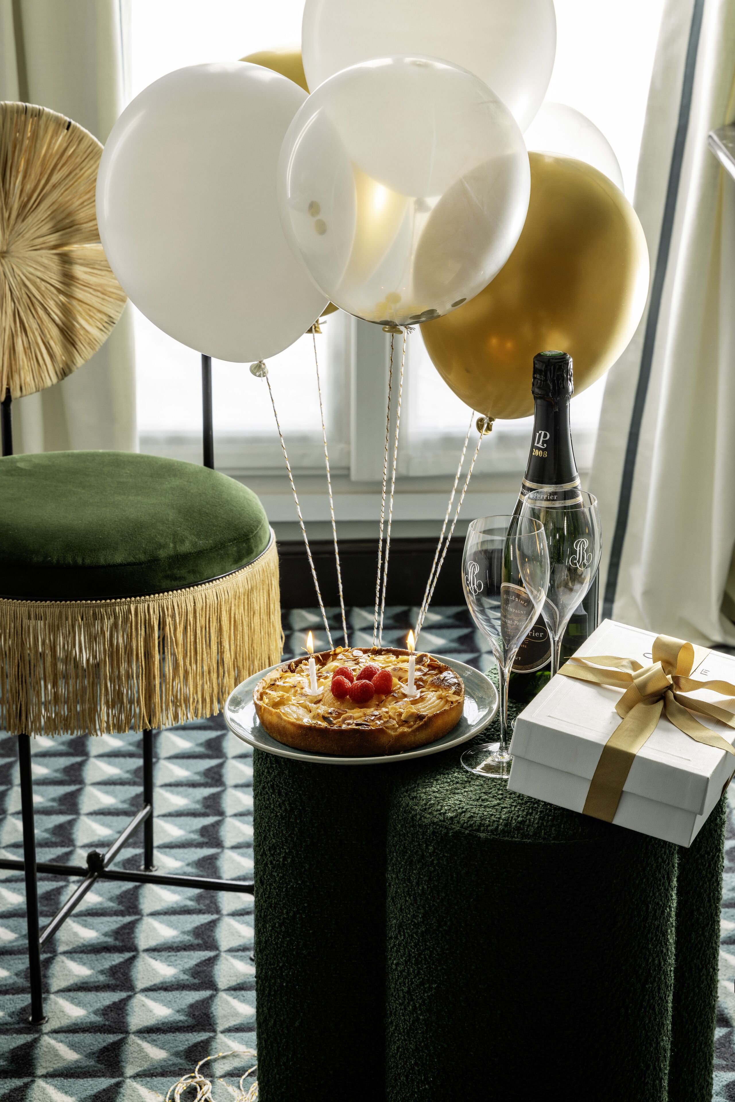 Een tafel met taart, champagne, ballonnen en een cadeaudoos.