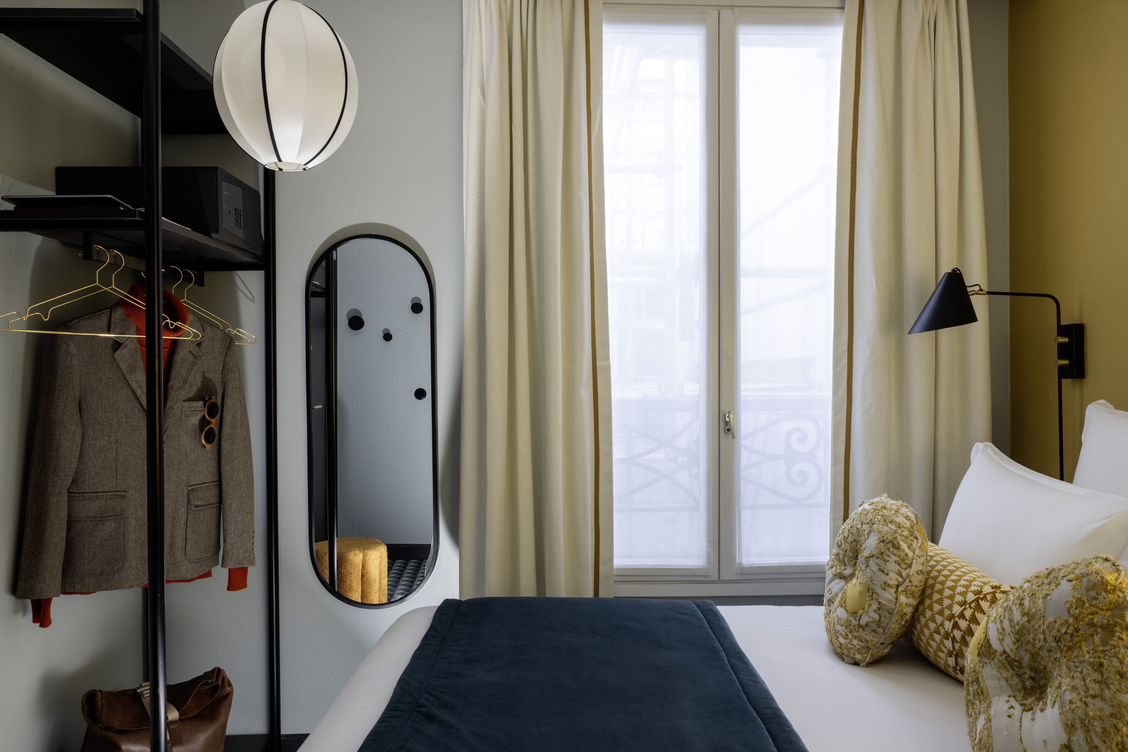 A hotel room with a bed, a mirror, a wardrobe, and a window with curtains.