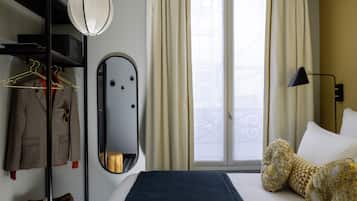 A hotel room with a bed, a mirror, a wardrobe, and a window with curtains.