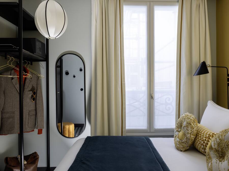 A hotel room with a bed, a mirror, a wardrobe, and a window with curtains.