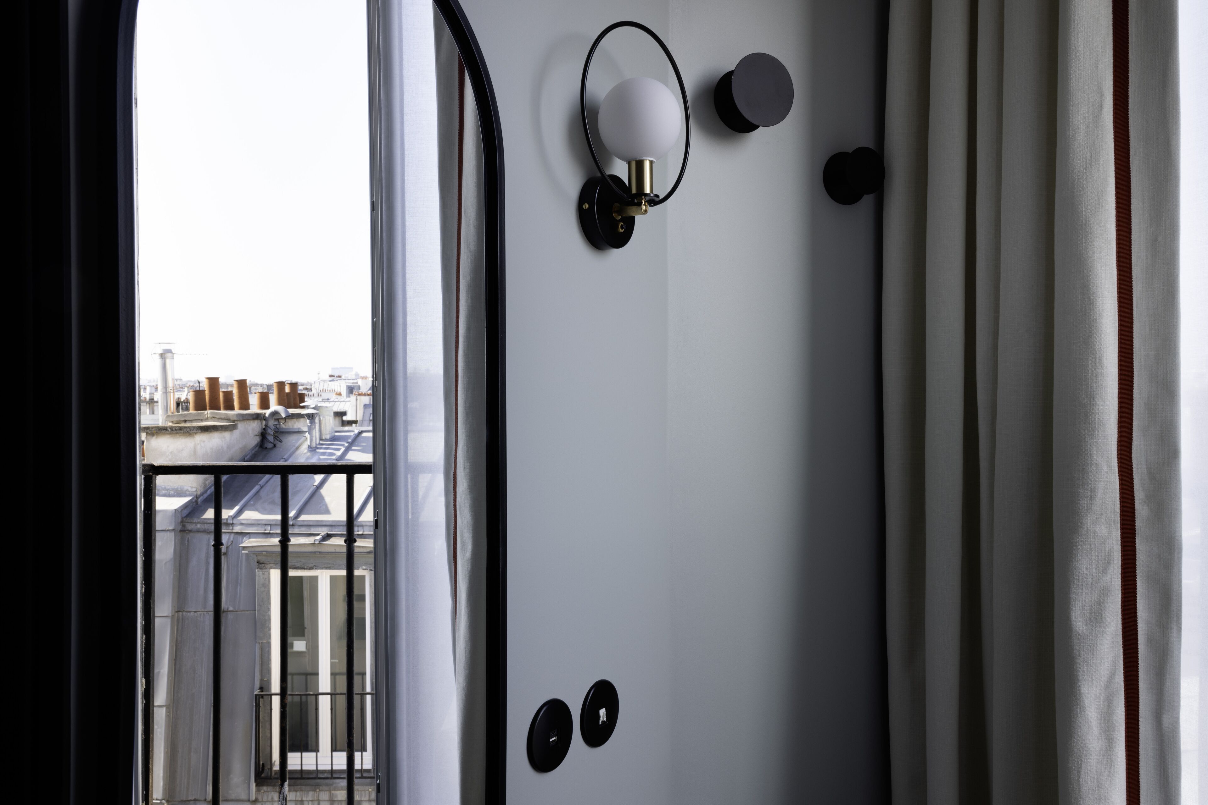A room with a view of the city through a window, a wall-mounted light fixture, and a door with two round handles.