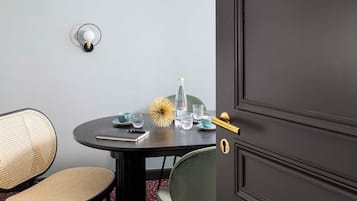 A room with a dark wooden door labeled "Le bureau," a round table with chairs, a hanging light fixture, and a wall-mounted light.