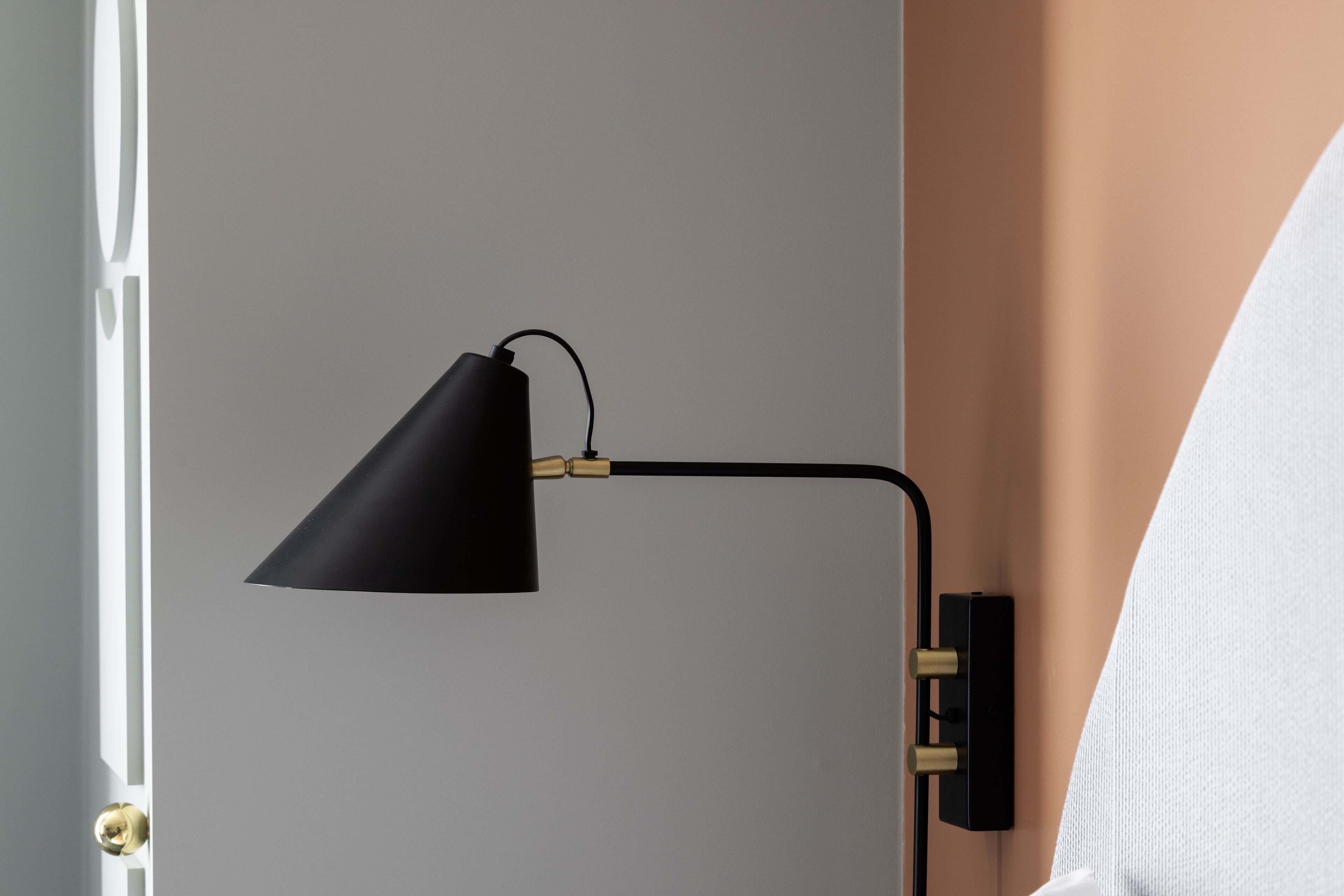 Een hoek van een kamer met een zwarte bureaulamp op een wandbeugel.