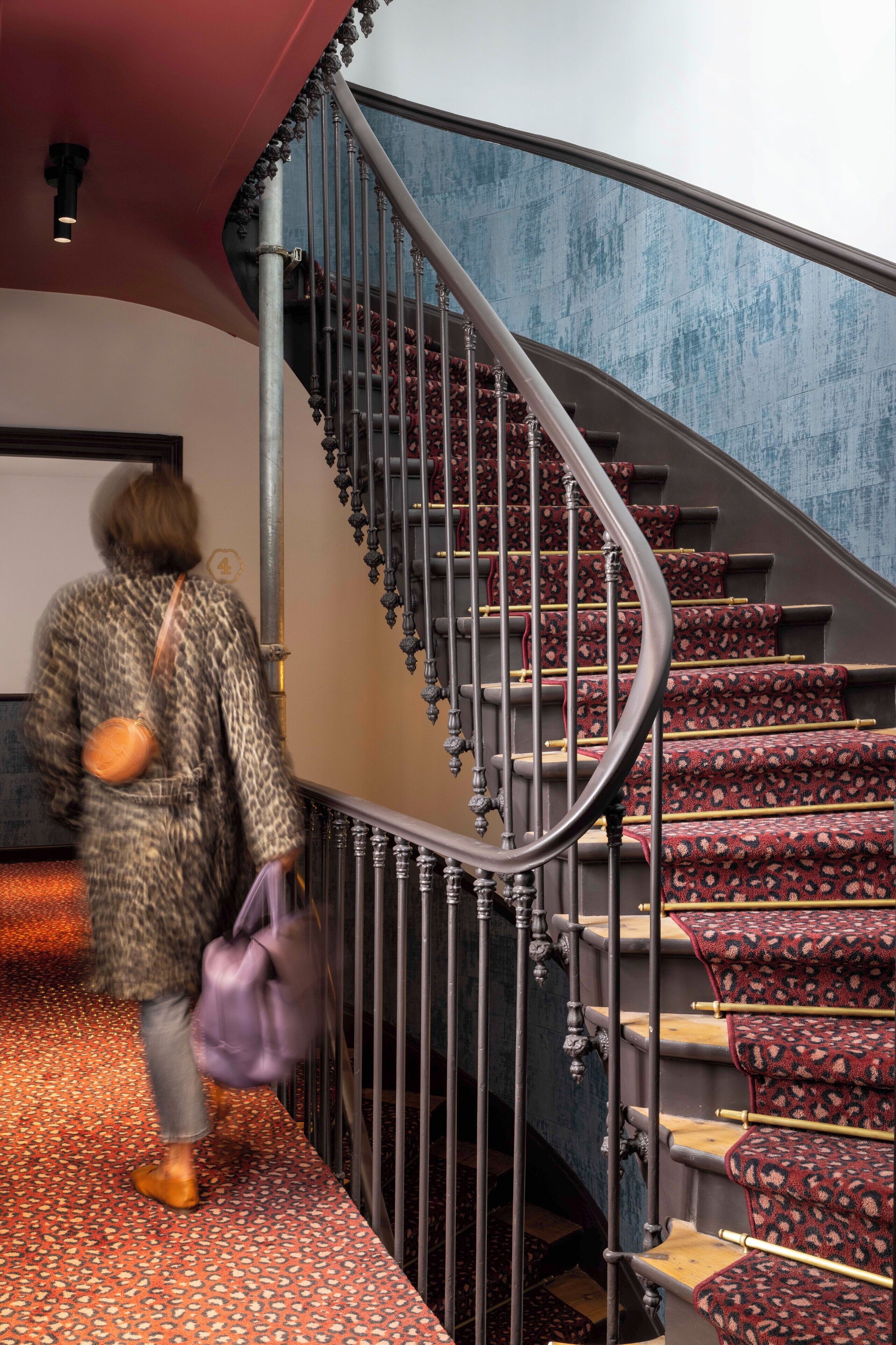 A person descending a spiral staircase with red carpeted steps and a metal railing.