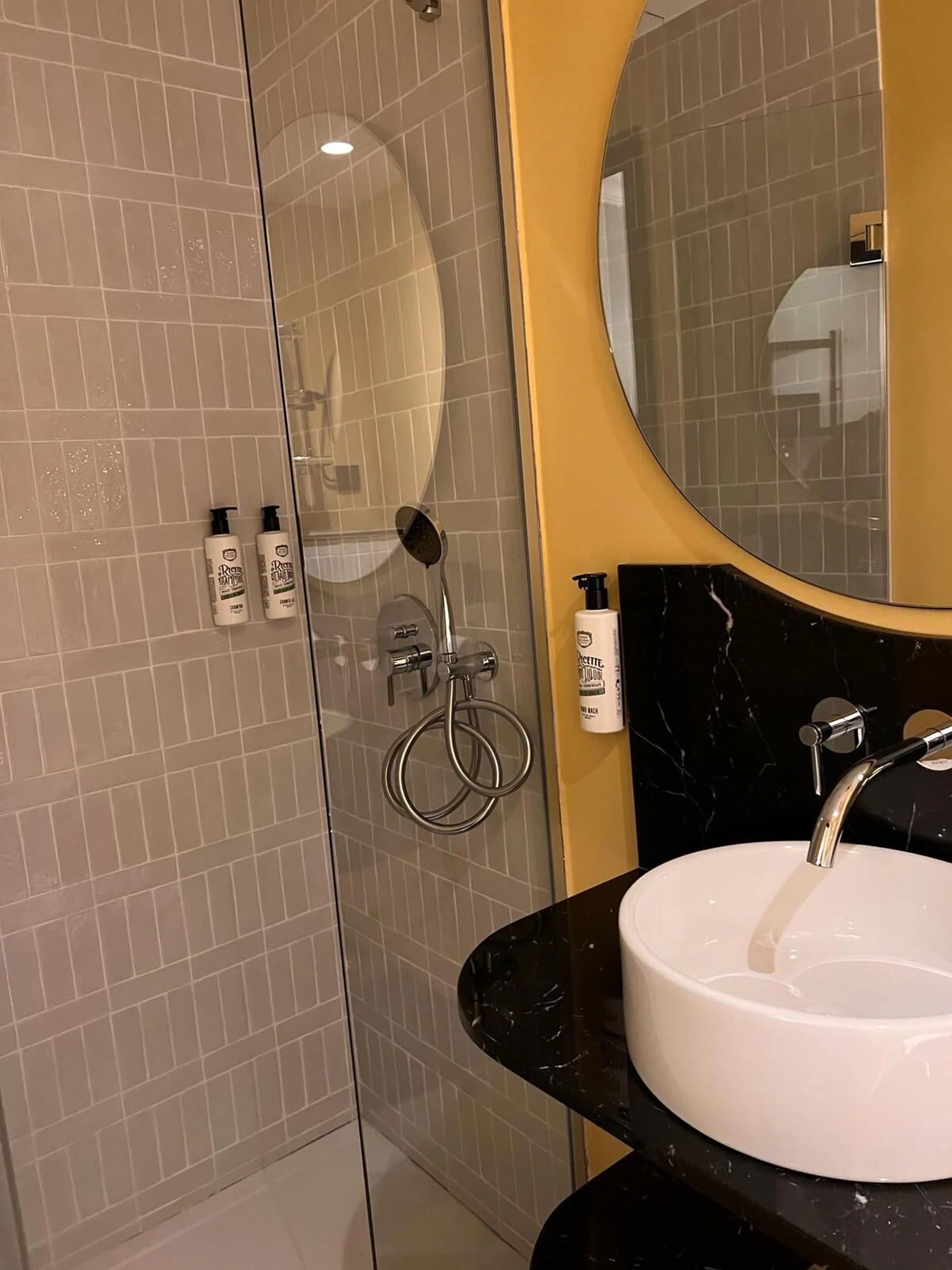 A modern bathroom with a glass-enclosed shower, a round mirror, and a black marble sink.