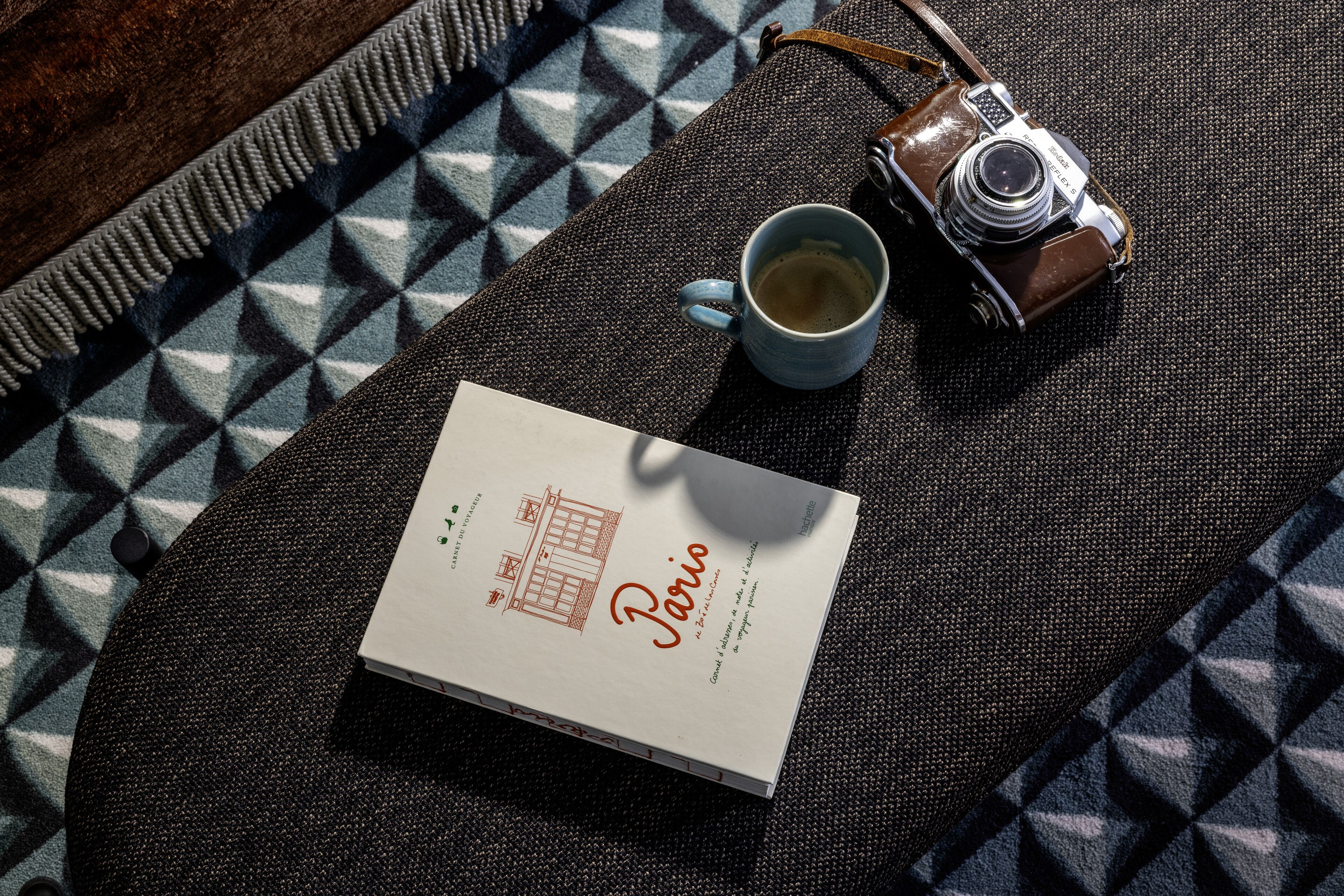 A book titled "Paris" on a textured surface with a camera and a cup.