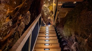 A wooden staircase in a cave with railings and lights. - Unique Cliff Hot Tub with Views | Mural | Sleeps 4 (Rogers)