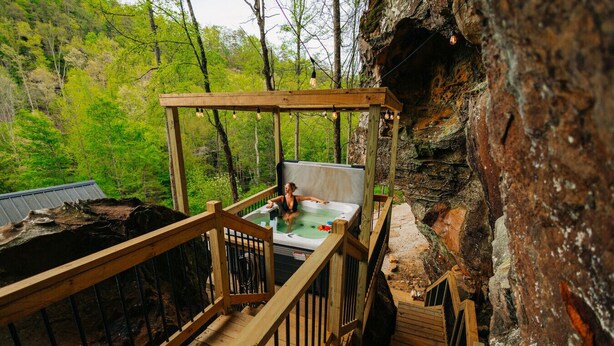A wooden deck with a hot tub and a wooden railing. - Unique Cliff Hot Tub with Views | Mural | Sleeps 4 (Rogers)