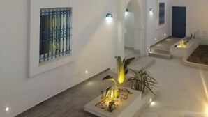 Un edificio blanco con varias ventanas y puertas, un patio con plantas y una entrada bien iluminada.